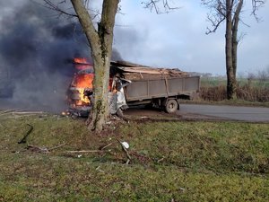 samochód ciężarowy stojący w poprzek drogi, który uderzył w drzewo, przód pojazdu w płomieniach
