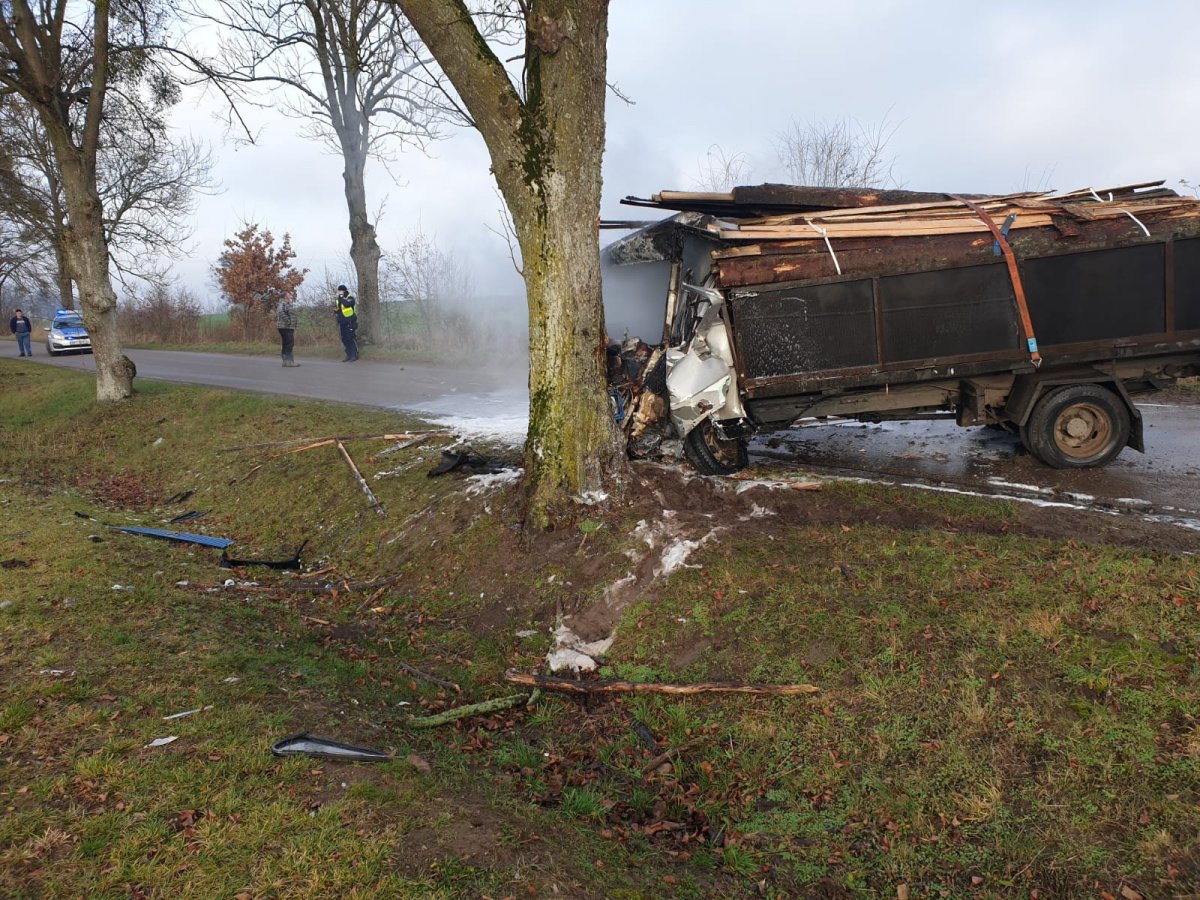 Ugaszony pojazd ciężarowy który uderzył przodem w drzewo w oddali trzech mężczyzn i radiowóz