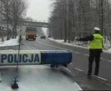 Policjant stojący na drodze za radiowozem z lizakiem w ręku, zatrzymujący samochód do kontroli