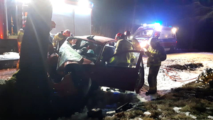 Służby ratunkowe stoją przy rozbitym pojeździe, w tle karetka pogotowia, wóz strażacki