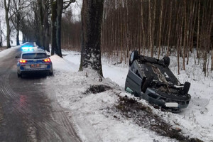 Po prawej stronie w rowie na dachu leży osobowe auto dalej na drodze stoi radiowóz na sygnałach w świetlnych