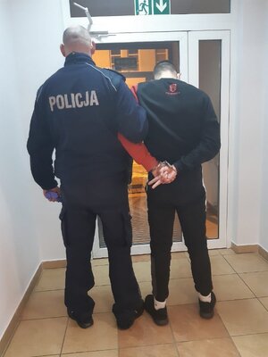 Policjant prowadzi osobę zatrzymaną, obaj są tyłem