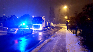 Po lewej stronie ulicy radiowóz na sygnałach świetlnych przed nim samochód ciężarowy