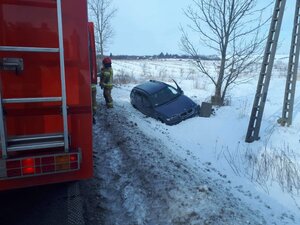 Samochód leżący w rowie po lewej stronie wóz strażacki i strażak
