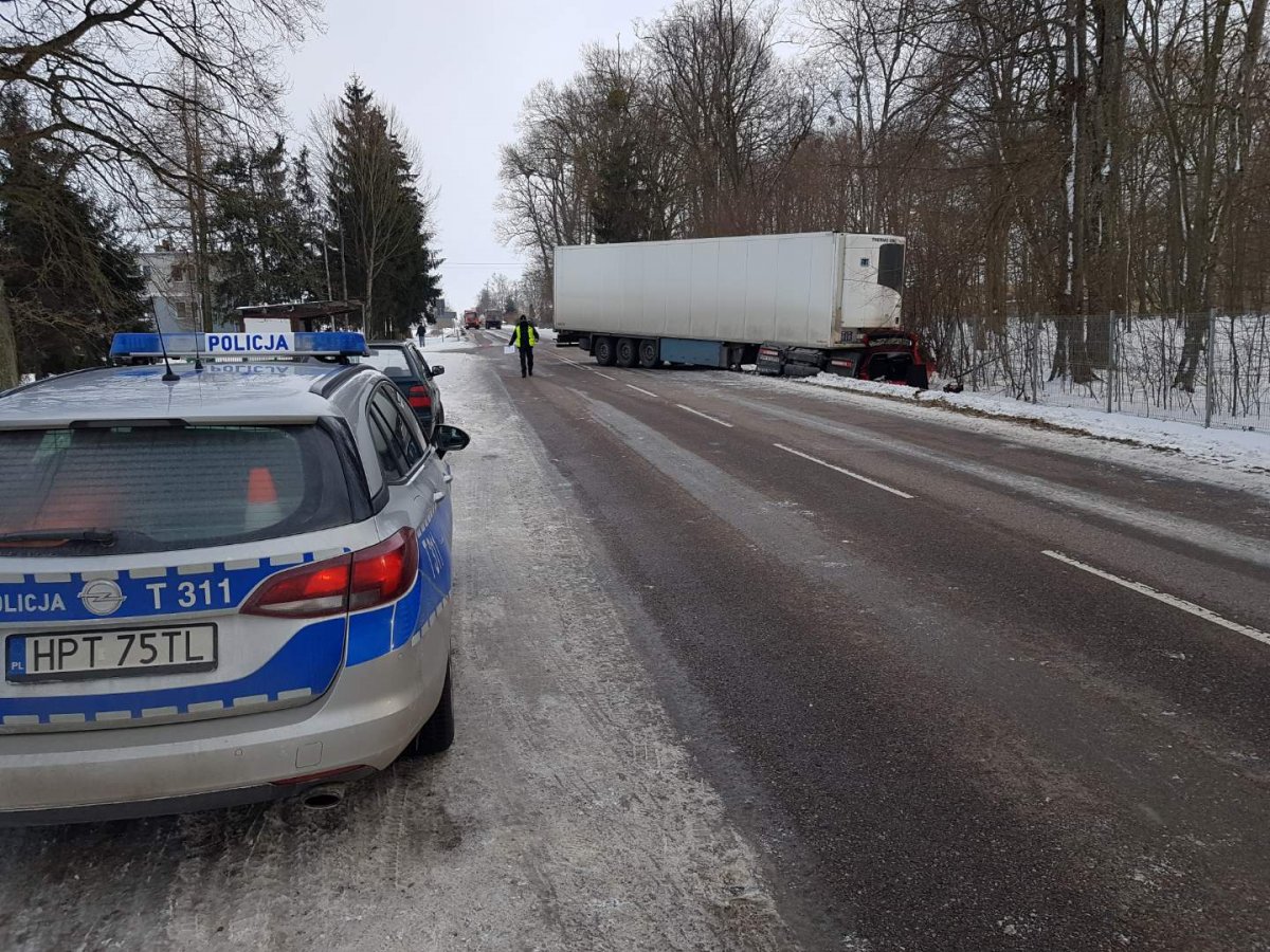 Po lewej stronie na poboczu stoi radiowóz po prawej samochód ciężarowy w rowie po środku drogi policjant