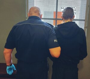 Policjant trzyma pod rękę osobę zatrzymaną