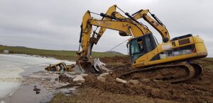 Rozlewisko wody z której wystaje dach spycharki na piachu przed rozlewiskiem stoi spychacz