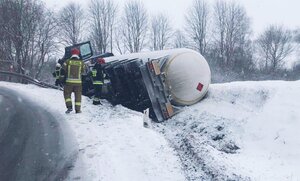 po prawej stronie drogi w rowie na boku leży cysterna, na drodze stoi dwóch strażaków