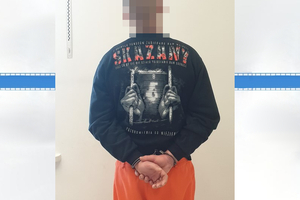 Jeden z zatrzymanych mężczyzn stojący twarzą do ściany z kajdankami założonymi na ręce trzymane z tyłu