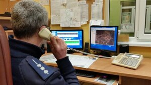Oficer dyżurny odbiera telefon siedząc przy biurku przed monitorami.