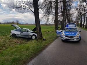 Rozbity pojazd stojący na poboczu, na drodze radiowóz na sygnałach świetlnych