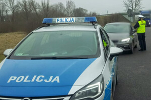 Policyjny radiowóz a za nim policjant przeprowadzający kontrolę samochodu osobowego