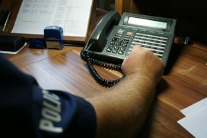 Ręka policjanta wyciągnięta w kierunku telefonu na biurku