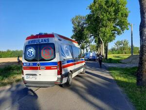 wzdłuż drogi stoi karetka, radiowóz i idący policjant