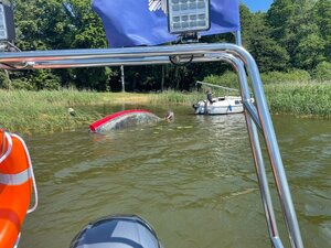 wywrócona łódź na jeziorze obok łodzi mężczyzna i kobieta stojąca na drugiej łodzi