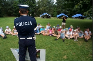 Policjant stojący przed dziećmi siedzącymi na trawie