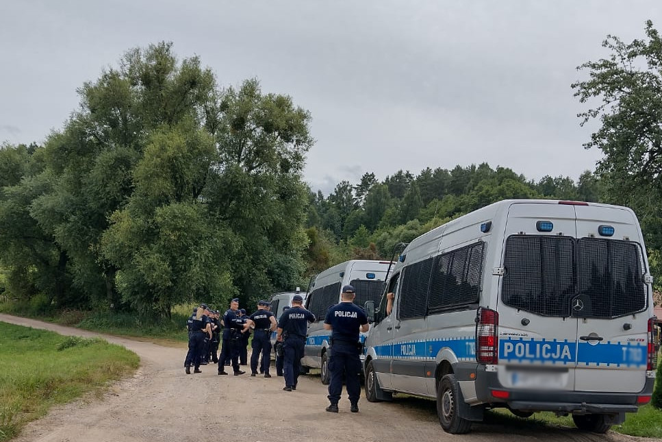 Radiowozy oraz policjanci na polnej drodze obok lasu i miejsca poszukiwań