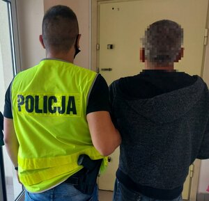 Policjant w kamizelce odblaskowej prowadzi osobę zatrzymaną