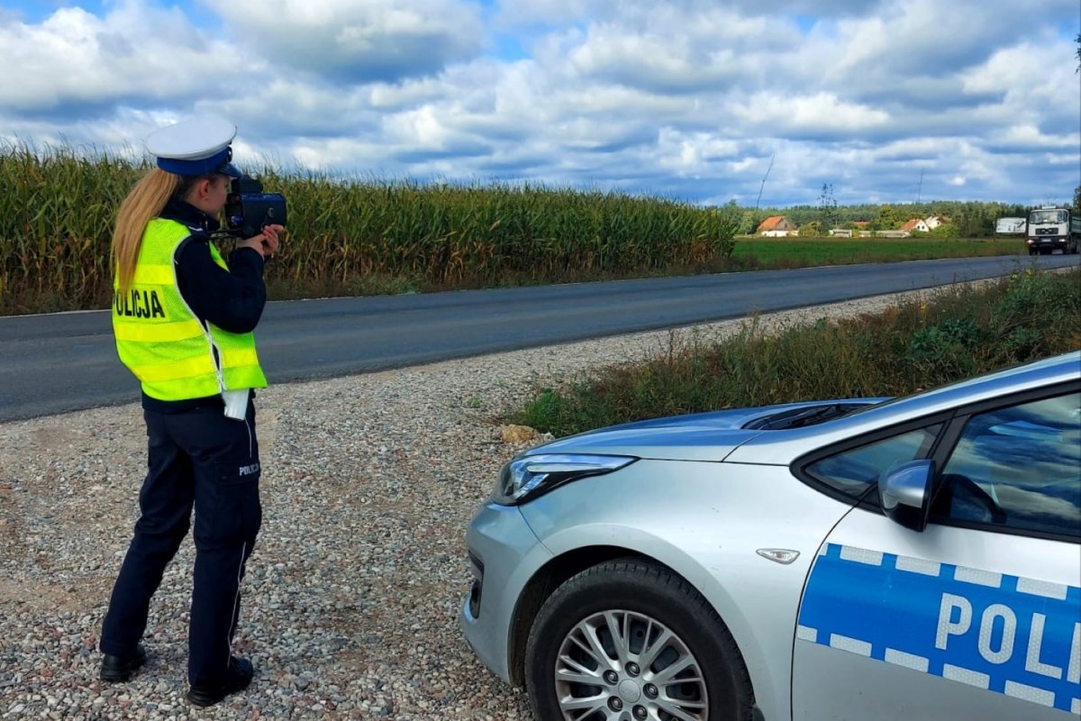 Policjantka podczas statycznego pomiaru prędkości, stojąca na poboczu obok radiowozu