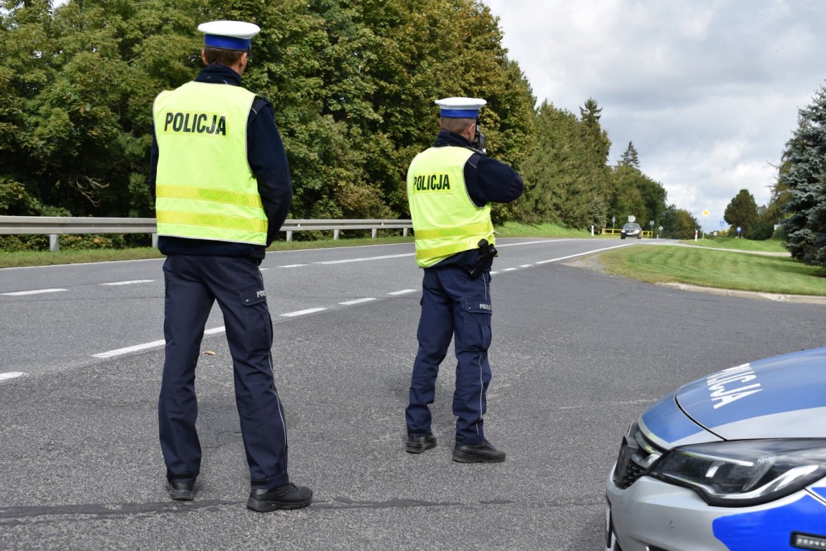 Policjanci prowadzący statyczny pomiar prędkości, stojący na drodze obok radiowozu