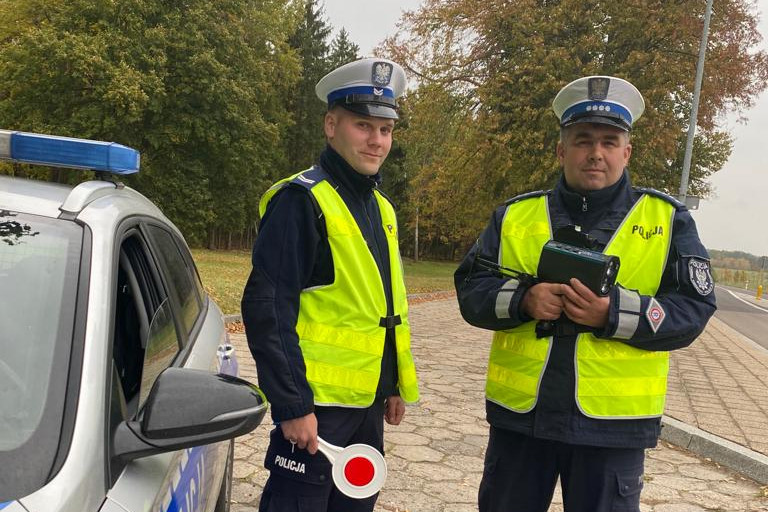 Policjanci w trakcie prowadzenia pomiaru prędkości stojący obok radiowozu.