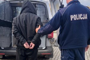 Zatrzymany mężczyzna prowadzony przez policjanta do radiowozu