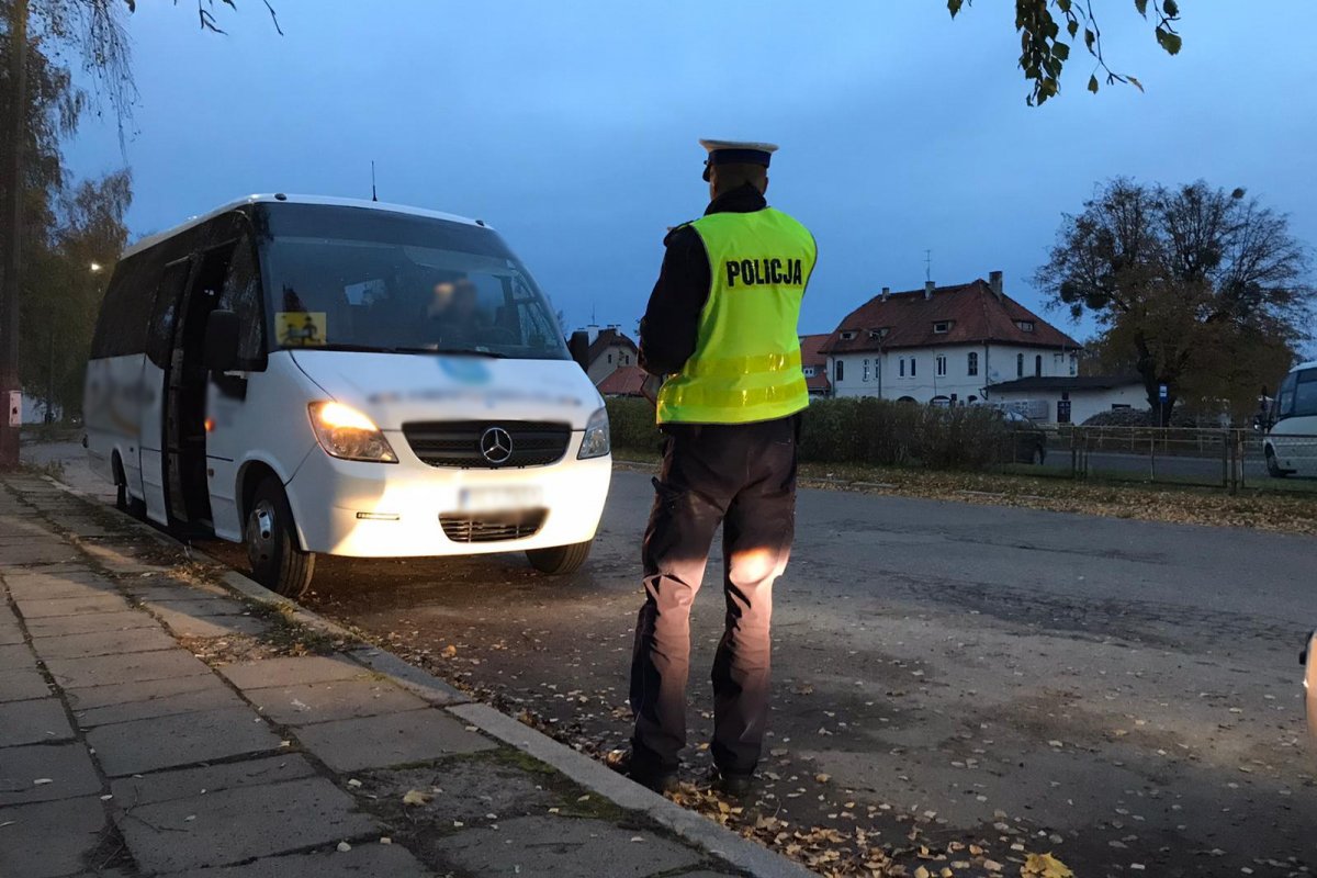 Policjant kontrolujący na parkingu oświetlenie busa przewożącego pasażerów