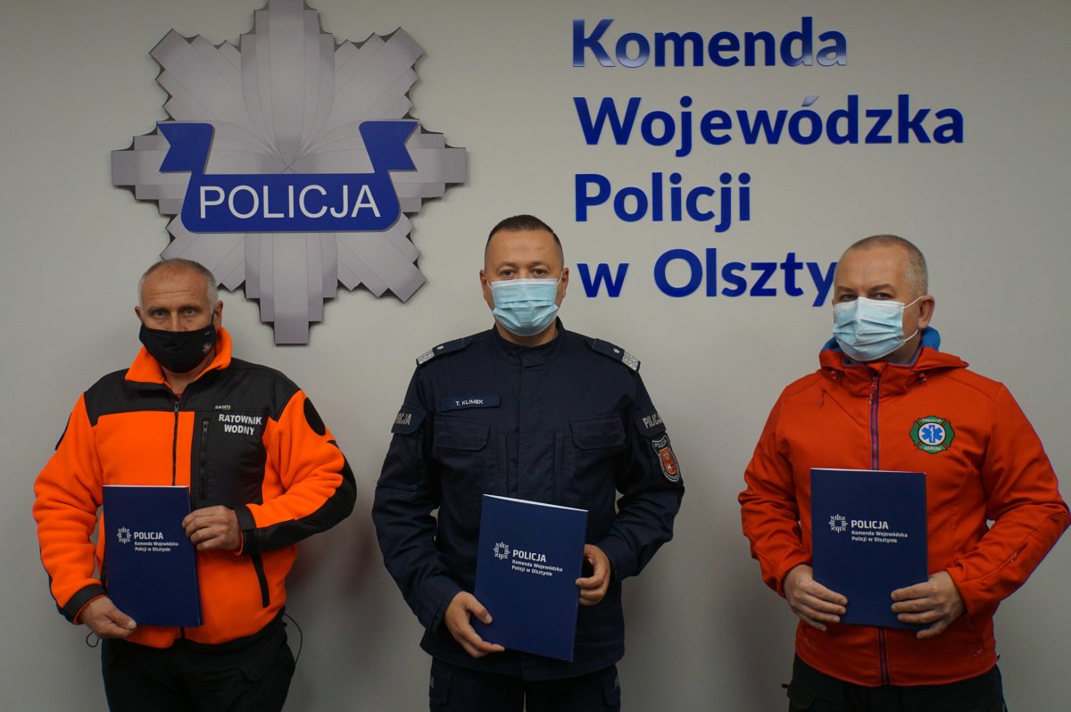 Sygnatariusze porozumienia stojący pod ścianą, na której znajduje się logotyp KWP w Olsztynie