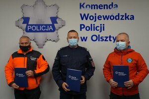 Sygnatariusze porozumienia stojący pod ścianą, na której znajduje się logotyp KWP w Olsztynie