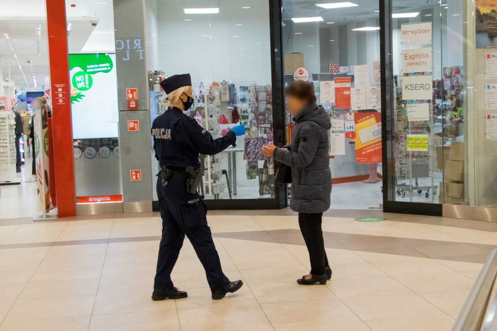 Policjanci w trakcie służby wręczają maseczki klientom centrum handlowego