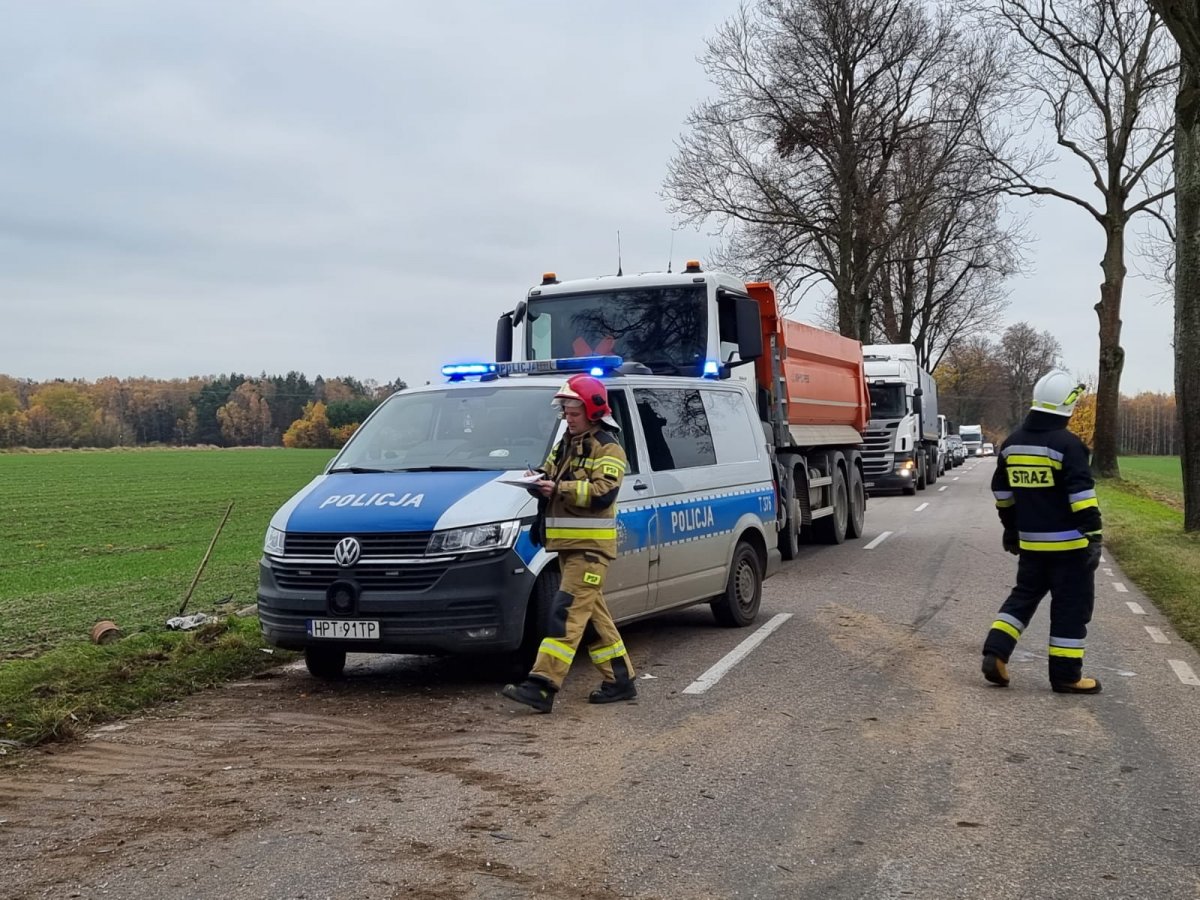 policyjny radiowóz i ciąg innych pojazdów stojące na drodze wojewódzkiej nr 542, obok radiowozu przechodzi strażak