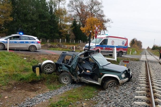 rozbity pojazd stojący przy torach kolejowych, dalej karetka i radiowóz