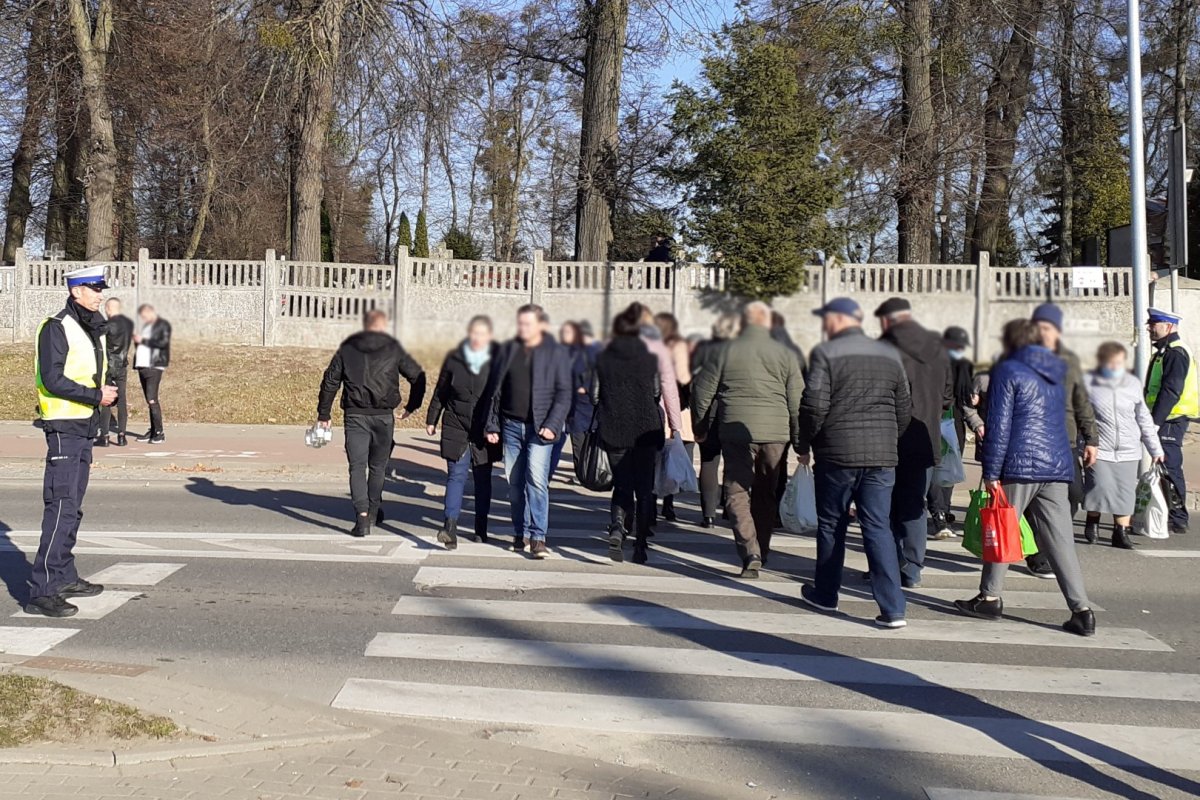 Funkcjonariusze podczas służby w powiecie bartoszyckim. Policjanci stojący po dwóch stronach przejścia dla pieszych, po którym przechodzą piesi