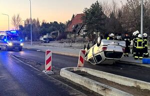 samochód leżący na jezdni kołami do góry, przy nim służby ratunkowe