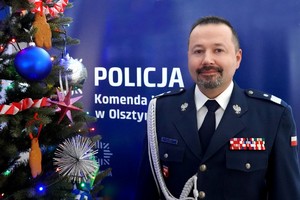 Nadinsp. Tomasz Klimek stojący obok choinki na tle napisu Komenda Wojewódzka Policji w Olsztynie