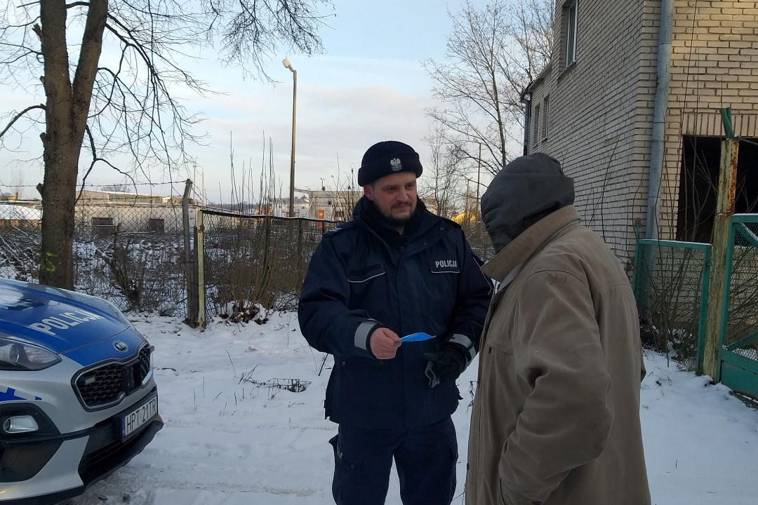 Policjant kontrolujący miejsce przebywania osób bezdomnych i rozmawiający z jedną z takich osób