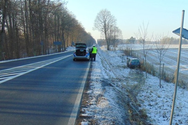 Radiowóz stojący na drodze obok kontrolowanego auta, które uszkodzone stoi w przydrożnym rowie