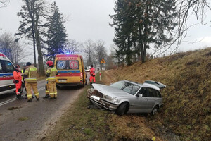 Miejsce zdarzenia drogowego. Policjanci i ratownicy wykonujący czynności na drodze. Rozbity samochód w przydrożnym rowie