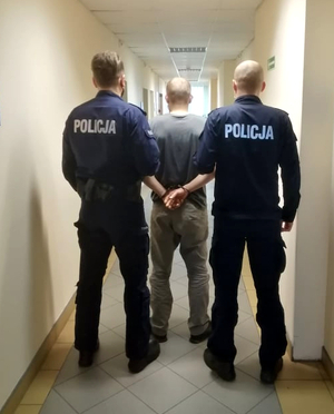 dwóch policjantów prowadzi osobę zatrzymaną