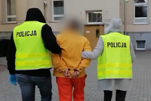 dwoje policjantów w kamizelkach odblaskowych prowadzi osobę zatrzymaną do sądu