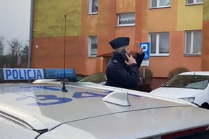 Policjant w trakcie kontroli izolacji. Stoi przy radiowozie i rozmawia przez telefon