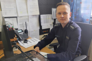 st. asp. Jacek Zbrzyzny siedzący w mundurze za biurkiem przed komputerem