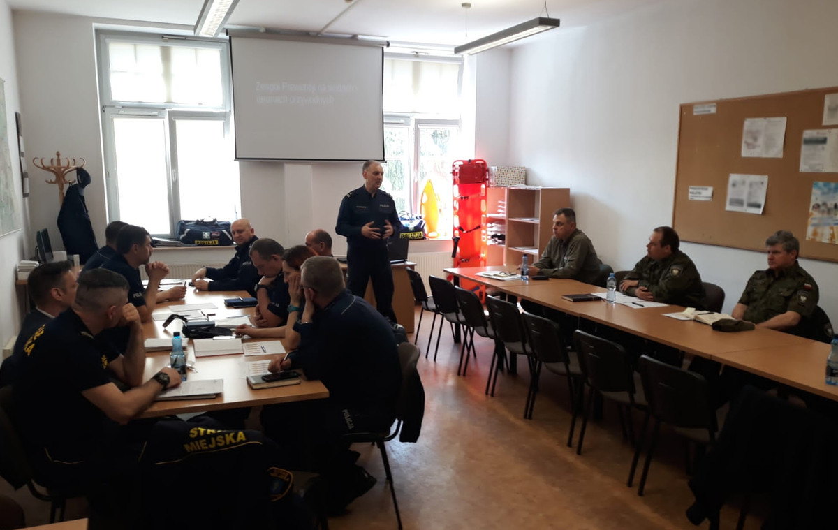 Spotkanie przedstawicieli służb w Olsztynie. Uczestnicy odprawy siedzą przy stołach.
