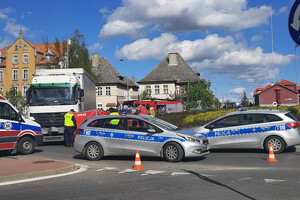 Miejsce zdarzenia drogowego. Rondo, na którym stoją radiowozu i ciężarówka oraz pracujący na nim policjanci i ratownicy wykonujący czynności