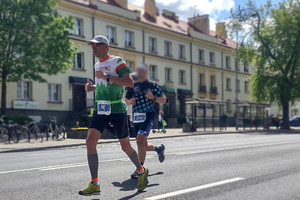 Dwóch mężczyzn w sportowym ubraniu biegnących ulicą. W tle budynek.