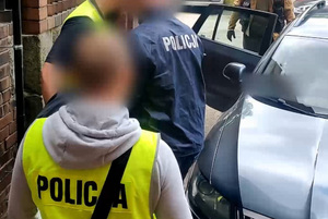 Zatrzymany mężczyzna prowadzony przez policjantów do radiowozu