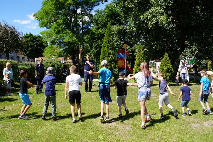 Dzieci na trawniku wykonują ćwiczenia pokazywane im przez policjanta