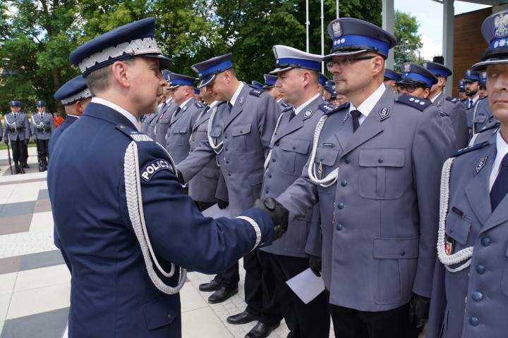 Awansowany policjant stojący w szeregu odbiera akt mianowania i gratulacje od komendanta