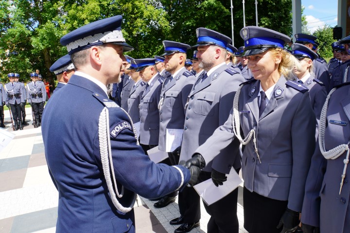 Awansowany policjant stojący w szeregu  odbiera akt mianowania i gratulacje od komendanta