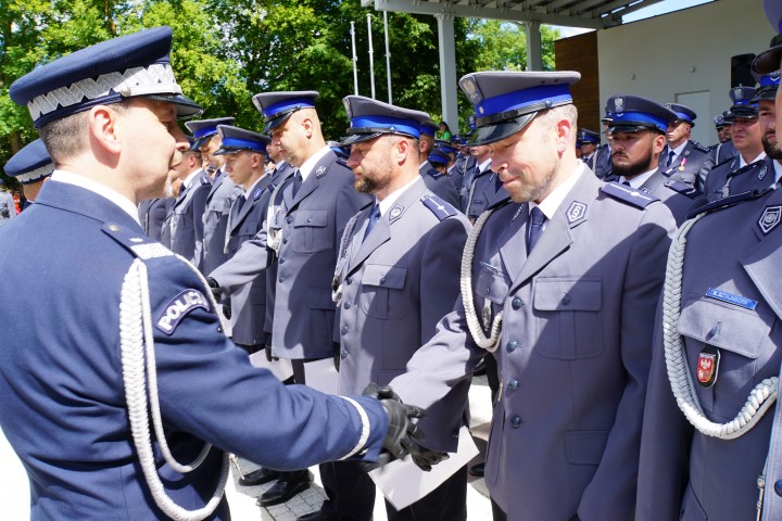 Awansowany policjant stojący w szeregu  odbiera akt mianowania i gratulacje od komendanta